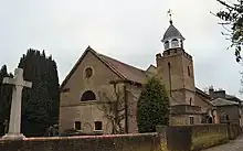 A small brick church surrounded by trees, with a war memorial in the foreground