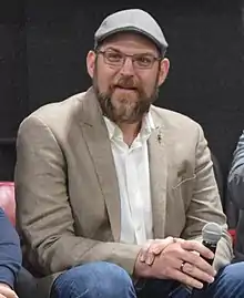 A 43-year-old man with a brown beard and a hat, smiling slightly to the left of the camera.