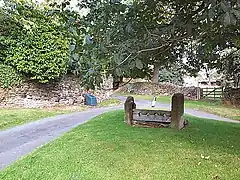 A small village green bounded by two roads, with a set of stocks on the grass