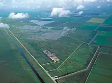 A color photograph taken from the air showing orderly sugarcane fields bordered by canals; to the south are the Everglades in a more natural state; in the center are a series of manmade cement ponds that act as stormwater treatment areas