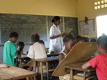 Students grouped around oversized slates in classroom as teacher observes