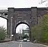 A brick arch over a road, with the start of an iron arch on the left.