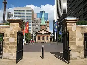 A recent photo. The church is seen framed by the gateposts of the nearby Barracks. Its steeple is seen against a backdrop of multi-storey buildings.