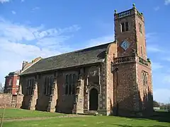 A brick church with a tower on the right incorporating two stone balustrades