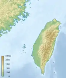 A topographical map of Taiwan, showing altitude with colours; green lowlands along the island's western edge with a spine of mountains down the center and east showing in various shades of brown