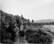 Passenger and goods train under rock ledge beside Tākaka River