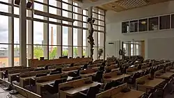 Interior view of a large meeting room, including rows of desks and chairs facing towards a large window