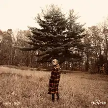 A sepia toned picture of Taylor Swift standing in a field. The background consists of trees.