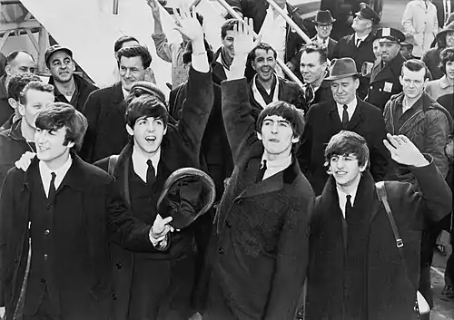 A black-and-white image of four men standing in front of a crowd of people at the bottom of an aeroplane staircase