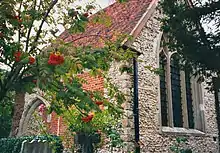 Part of a stone and brick chapel with a red tiled roof seen from an angle