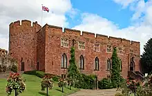 Red stone built castle with turret on the left and flowers lining the approach road