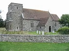 A flint church with a red tiled roof and a short west tower