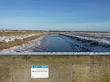 Tidal river between snowy banks, seen from an overbridge with a helpful notice