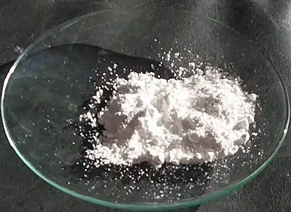 Watch glass on a black surface with a small portion of white powder