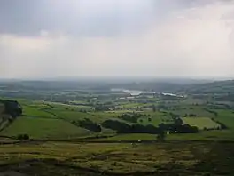 a wide landscape shot of green fields with a lake in the distance