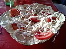 A tlayuda topped with tomato and strings of quesillo Oaxaca