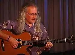 Cox performing at the Grahamstown National Arts Festival, South Africa, in June 2005. He is pictured playing a long-scale-length acoustic baritone guitar custom-made for him by Ian Corr.