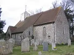 A flint church with a tiled roof and a small white weatherboarded bellcote