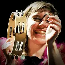 Garbus smiling with make-up on her face, hitting a tambourine