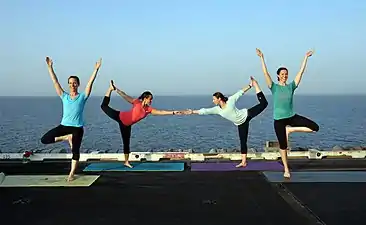 A US Navy yoga display on the flight deck of USS George H.W. Bush, using Vrikshasana and Natarajasana, 2014