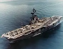 Medium-size aircraft carrier with numerous aircraft on its flight deck.