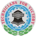 Circular emblem with a knights helmet facing forward layered over a silver grey gear, layered over a oriental blue gridline sphere, surrounded by a green wreath at the bottom and the words "TECHNICIANS FOR VICTORY" in red wrapping around the top and sides of the emblem