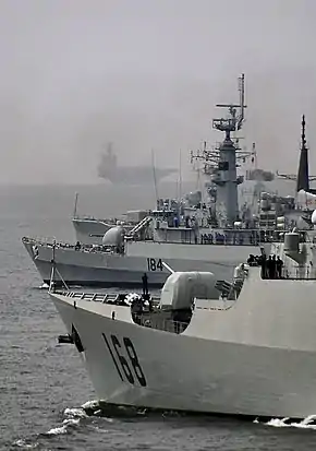 PNS Badr anchored with the Chinese Navy Guangzhou, the American USS Lake Champlain, and USS Theodore Roosevelt (the aircraft carrier in background) during the naval drill, Aman-09, hosted by Pakistan in the Indian Ocean in 2009.