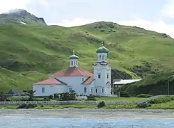 alt=Photograph of the Church of the Holy Ascension on a sunny day, with red roofs, green onion domes, and a small churchyard.