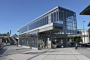 A two-story glass and metal building with stairs and escalators visible from a canopied entrance.