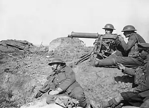 Four men in a barren landscape with a tripod-mounted machine gun