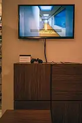 A television screen placed above a placard with a controller next to it. The television is displaying part of the "Confusion Ending" of the remake, in which the player is told to follow a painted yellow line through the office.