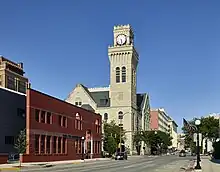 A gray brick Romanesque Revival building with a signature clock tower