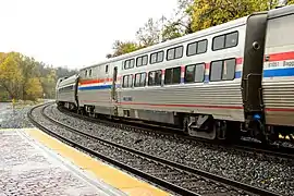 A stainless steel passenger rail car with red, white, and blue stripes of equal width on the side