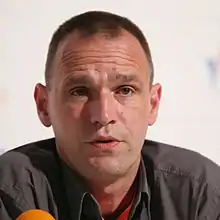 A middle-aged man with short black hair talking at a press conference.