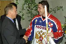 Vladimir Putin and Pavel Bure are shaking hands.