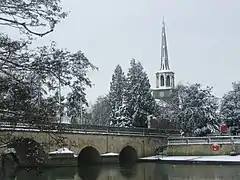 An arched bridge beyond which is a tower with a belfry and spire