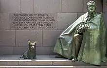 "A green statue of a man wrapped in a cloak alongside a statue of a Scottish Terrier."