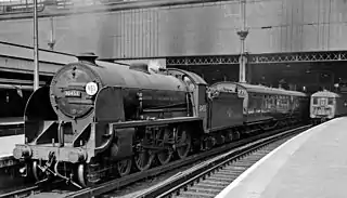 A steam locomotive waiting with its train at a station