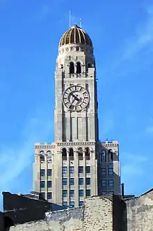 Clock and dome on the building's upper stories. The facade is made of beige stone, while the dome is a darker color.