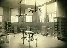 A black and white photo of a small bed in a large room