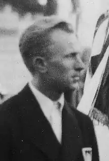 A young man visible from the chest up, looking to his left, and wearing a suit and tie