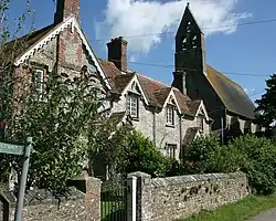 A row of cottages, partially obscured by vegetation. In the background is the bell tower of a much larger building.