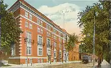 Exterior of a five-storey red brick building and street scene including a trolley car