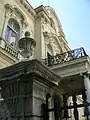 The wrought iron railings of the balcony above the veranda