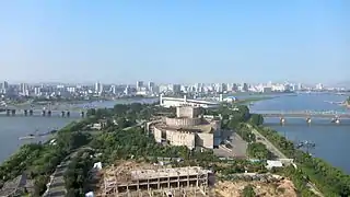 Yanggak Island in August 2012; from front to rear: new health complex's construction site, International Cinema Hall, Yanggak Bridge, and Yanggakdo Stadium