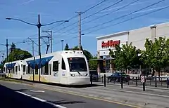 A train running along the street median with Fred Meyer supermarket in the background