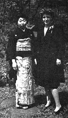 Photograph of a woman in a kimono standing beside a woman in a business suit.