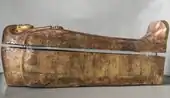 Side view of gilded coffin shaped like a mummy